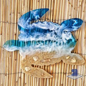 Peut inclure: Décoration murale en forme de tortue en résine bleue et blanche, représentant une scène de plage. Le design comprend une vague, du sable et des coquillages. Le nom "Jessugar" est écrit sur la vague. Fond en natte de bambou.
