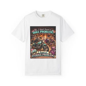 Puede incluir: Una camiseta blanca con un estampado gráfico de varias motocicletas en un garaje. El texto dice: "No, I don't have a BIKE PROBLEM. I have a STORAGE PROBLEM." El diseño incluye flores coloridas y un casco de color rosa.