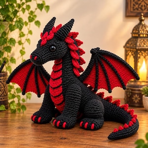 May include: A crocheted dragon plush toy featuring a black body with vibrant red accents on its wings, chest, and along its back. The creature has large dark eyes, pointed horns, and red claws on its feet, crafted with detailed yarn stitching.