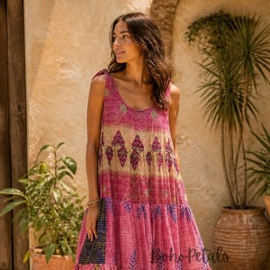 May include: A sleeveless tiered midi dress in shades of pink, featuring a scoop neckline, tie-shoulder straps, and a multi-patterned fabric design with visible stitching. The text Boho Petals is printed on the lower section of the dress.
