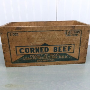May include: A wooden crate with a green and white label that reads "Libby's Corned Beef, Product of Brazil, Libby, McNeill & Libby, U.S.A., Distributors". The crate is labeled with "2 Doz. 12 oz. Tins 340 Grm."