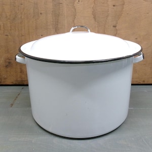 May include: A large white enamel stockpot with a matching lid. The pot features a smooth white finish, a thin black rim around the top edge and lid, and two small white side handles. The lid has a small, simple metal handle on the top center.