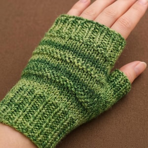May include: A fingerless glove featuring a variegated green knit pattern with horizontal ribbed sections. The hand covering displays a blend of light and dark green yarn tones, constructed with a textured stitch that extends from the wrist to the knuckles.