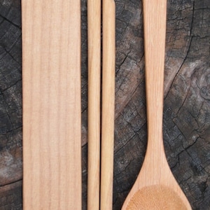 May include: A set of wooden kitchen utensils, including a spoon, chopsticks, and a rectangular serving utensil. The utensils are made of light brown wood and have a natural finish.