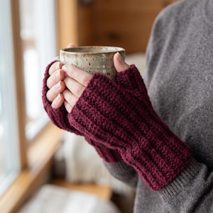 May include: A pair of deep burgundy fingerless gloves featuring a thick, ribbed knit texture. The gloves are crafted from yarn and extend from the knuckles down to the wrists, providing coverage while leaving the fingers exposed for movement.