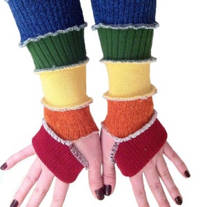 May include: A pair of rainbow fingerless arm warmers made from recycled sweaters. The arm warmers are layered in the colors of the rainbow, starting with blue, green, yellow, orange, and red.