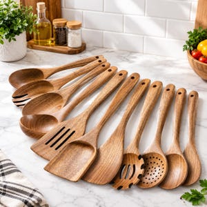May include: A set of eleven wooden kitchen utensils arranged in a fan shape on a marble surface. The collection includes various spoons, spatulas, a slotted turner, a pasta server, and a skimmer, all featuring a natural brown wood grain finish.