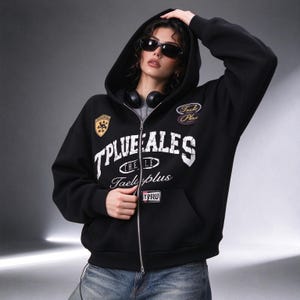 以下が含まれることがあります： TPLUEEALES THE LE Taeleplusと書かれた白いかすれた文字が特徴の黒いジップアップパーカー。右胸には黄色い盾の形のワッペン、左側には暗い楕円形のワッペン、ポケットには小さな長方形のタグが付いています。