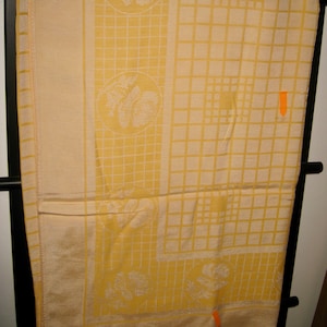 May include: A yellow tablecloth with a white grid pattern and floral designs. The tablecloth is hanging on a black rack.