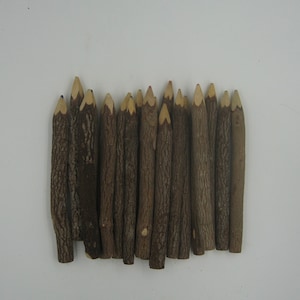 May include: A group of 18 brown wooden pencils with sharpened points. The pencils are arranged in a row, with the points facing up.