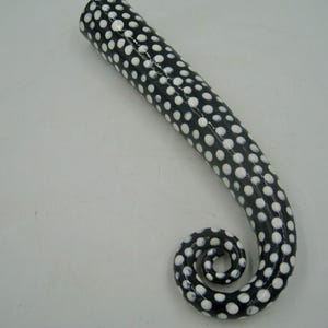 May include: A black tentacle-shaped decorative object with white polka dots. The tentacle curves into a spiral at the end. The object is on a white surface.