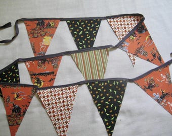 May include: A fabric bunting banner featuring triangular flags in various patterns including orange with skeletons and pumpkins, black with green bats, brown and white checkered prints, and green striped designs, all connected by a dark gray ribbon.