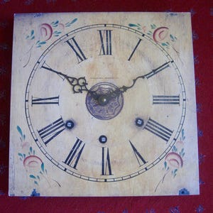May include: Square antique clock face with black Roman numerals and hands. The clock face is cream-colored with floral accents in pink, green, and blue. The clock face has the text "OTHERMORE, ROCHESTER, N.Y."