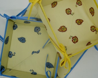 May include: Two fabric storage baskets with blue and yellow trim. The larger basket has a yellow trim and a floral pattern. The smaller basket has a blue trim and a floral pattern.