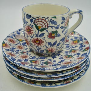 May include: A set of four white ceramic teacups and saucers with a floral pattern in blue, red, green, and yellow.