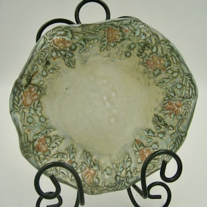 May include: A ceramic bowl with a green and brown floral design. The bowl is on a black metal stand.