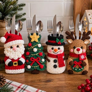 May include: Four crochet cutlery holders shaped like a Santa Claus, a Christmas tree, a snowman, and a reindeer. Each holder contains a silver fork, knife, and spoon. The figures feature festive colors including red, white, green, and brown yarn.