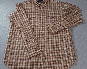 May include: A long-sleeve button-down shirt featuring a brown, tan, and white plaid pattern. The shirt includes a pointed collar, two chest pockets with snap closures, and a front placket with metal snap buttons. The label reads Polo Ralph Lauren.