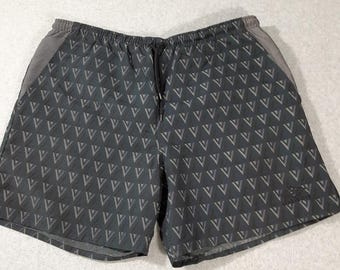 May include: Dark gray athletic shorts featuring an all-over repeating pattern of light gray triangles. The shorts have an elastic waistband with a black drawstring and solid gray side panels. A small logo is visible on the lower right leg.