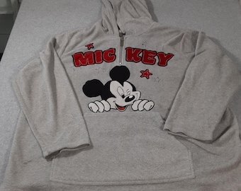 May include: A light gray hooded sweatshirt featuring a half-zip closure and a large graphic of Mickey Mouse. The text MIC KEY is printed in bold red letters above the character, accented by small red and outlined star shapes.