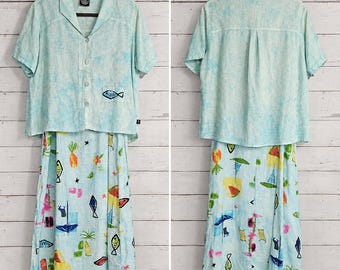 May include: A two-piece set featuring a light blue, mottled-texture short-sleeve button-down shirt with a small fish embroidery on the pocket, paired with a matching midi skirt decorated with colorful prints of fish, fruit, and beach items.