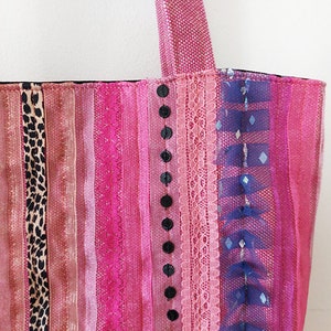 May include: A pink and black striped tote bag with a variety of fabrics and textures, including lace, sequins, and ribbon.