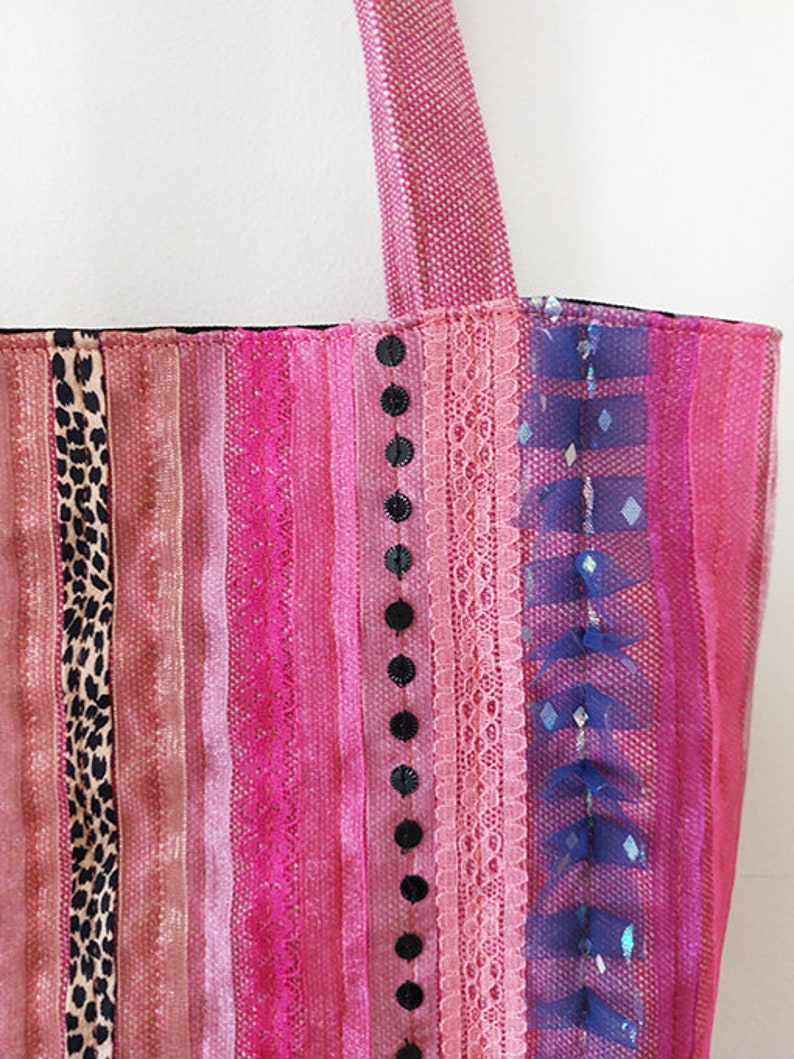 May include: A pink and black striped tote bag with a variety of fabrics and textures, including lace, sequins, and ribbon.