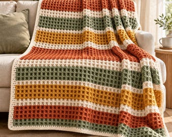 May include: A crochet blanket featuring a waffle stitch pattern with horizontal stripes in burnt orange, cream, sage green, and mustard yellow. The rectangular textile has a textured grid design and is draped over a sofa.