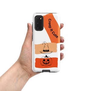 Puede incluir: Una funda de smartphone blanca con una franja diagonal naranja con el texto negro Creep it Cute, una pincelada horizontal beige con un sombrero de bruja en línea negra y una pincelada naranja con una calabaza de Halloween en línea negra.