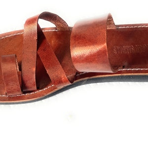 May include: Brown leather sandals with a toe loop and multiple straps. The sandals have a black sole and white stitching around the edges. The brand name "VOLCANO SANDALS" is visible on the footbed.