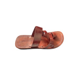 May include: Brown leather sandal with multiple straps and a toe loop. The sandal has a stitched sole and the text "HOLYLAND SANDALS" is visible. The size is marked as 36.