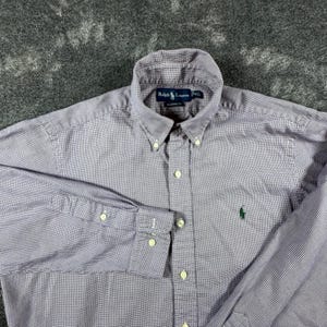 May include: A long-sleeve button-down shirt in a purple and white micro-check pattern. The shirt features a button-down collar, a front button placket, and a green embroidered logo on the chest. The interior label reads Ralph Lauren.
