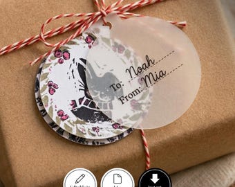 Puede incluir: Una caja de regalo marrón atada con cordel rojo y blanco, con dos etiquetas circulares. Una etiqueta es translúcida con el texto To: Noah y From: Mia. La otra etiqueta presenta un diseño de corona floral con bayas rosas y detalles negros.