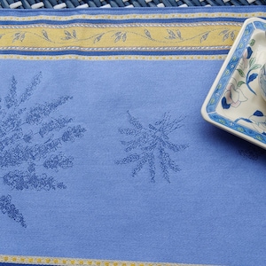 May include: Two blue placemats with yellow and white trim and a floral pattern. The placemats are on a woven blue and white surface. "Shot on OnePlus x Hasselblad" is printed on the surface.