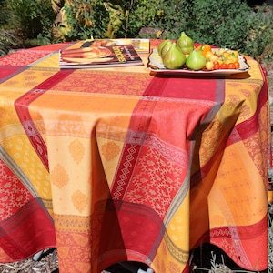 Puede incluir: Una mesa redonda con un mantel a cuadros rojo, naranja y amarillo. Un plato de higos y tomates se encuentra sobre la mesa, junto con un libro de cocina.