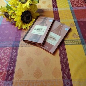 May include: Two wine books with yellow and red covers on a patterned tablecloth. The books are titled "Bandol" and "Beaune" with the author's name, David Cobbold, printed on the front.