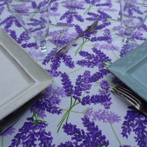 May include: A white tablecloth with a lavender floral pattern. Two clear glass goblets and two plates are set on the table. One plate is white and the other is light blue.