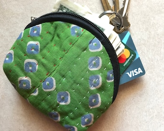 Op de afbeelding: Een groene stoffen muntbeurs met een zwarte rits en een blauw-wit patroon. De beurs is open en bevat contant geld, creditcards en sleutels.
