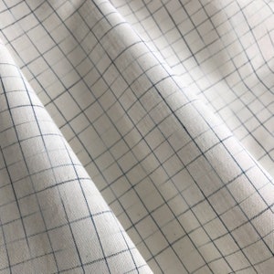 Könnte beinhalten: Weißer Stoff mit einem blauen Gittermuster. Der Stoff ist gefaltet und hat einen leichten Glanz.