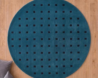 May include: A circular teal rug featuring a repeating grid pattern of small, solid black squares across its surface. The rug is positioned on a light brown wooden floor, with the text TheHandRugsCo visible in the bottom center area.