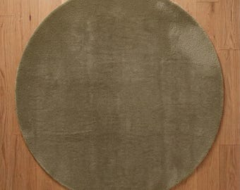 May include: A circular area rug in a solid olive green color with a short, dense pile texture. The rug features a simple, clean-edged round shape that lies flat, showcasing a uniform surface appearance throughout the entire piece.