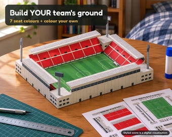 Könnte beinhalten: Ein Papiermodell eines Fußballstadions mit roten Sitzen und grünem Spielfeld, ausgestattet mit vier Flutlichtmasten. Der Text lautet: Build YOUR team's ground, 7 seat colours + colour your own. Enthält bedruckte Bögen, ein Metalllineal und ein Bastelmesser.