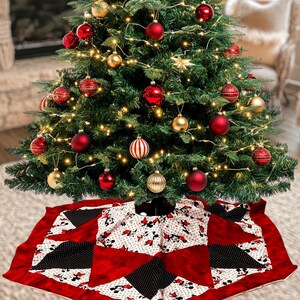 May include: A decorated Christmas tree with red and gold ornaments and string lights. A red, white, and black tree skirt with a Mickey Mouse pattern is beneath the tree. The tree is in front of a fireplace.