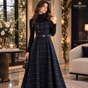 May include: A dark navy blue plaid sleeveless dress with a brown belt and two buttons on the bodice, worn over a black long-sleeve turtleneck top. The dress features a full-length skirt and is paired with a small black handbag. ZellaWardrobe logo.