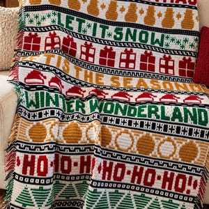 May include: A white crochet throw blanket featuring horizontal bands of red, green, and gold holiday motifs and text. Patterns include snowmen, gift boxes, Santa hats, ornaments, and trees, with text reading MERRY CHRISTMAS, LET IT SNOW, TIS THE SEASON, WINTER WONDERLAND, and HO-HO-HO.