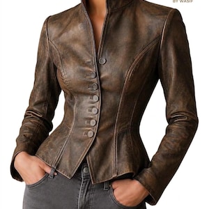 Könnte beinhalten: Eine braune Lederjacke mit Used-Optik, hohem Kragen, langen Ärmeln und einer Knopfleiste mit sechs sichtbaren Knöpfen auf der Vorderseite. Die Jacke hat eine taillierte Passform mit ausgestelltem Schößchen. Der Text lautet LEATHER STORE BY WASIF.