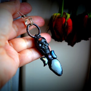 May include: A silver chain necklace with a black skull pendant and a clear crystal with iridescent accents.