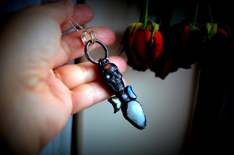 May include: A silver chain necklace with a black skull pendant and a clear crystal with iridescent accents.