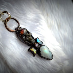May include: A silver chain necklace with a copper pendant featuring a skull, moonstone, and iridescent stones.