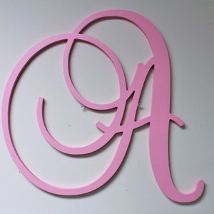 May include: A large, pink, wooden letter A in a cursive font. The letter is mounted on a white wall.